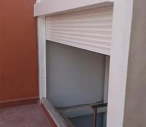 Hay una persiana blanca en una ventana al lado de una puerta.