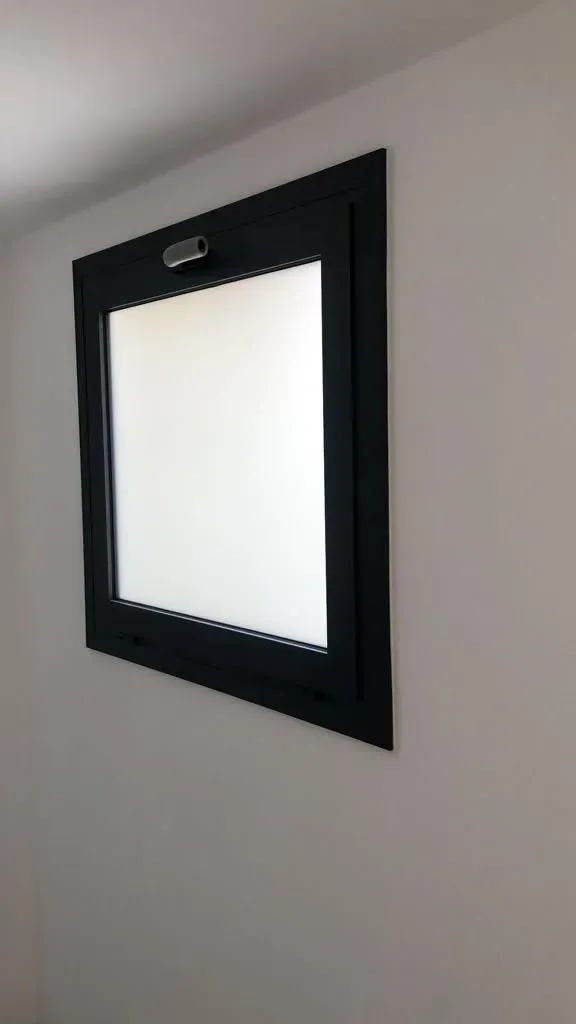 Una ventana cuadrada con un marco negro cuelga de una pared blanca.