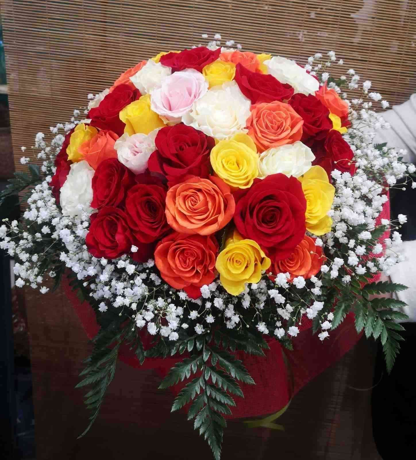 Un vibrante ramo de rosas rojas, naranjas, amarillas y blancas, adornado con paniculata y hojas de helecho verde.