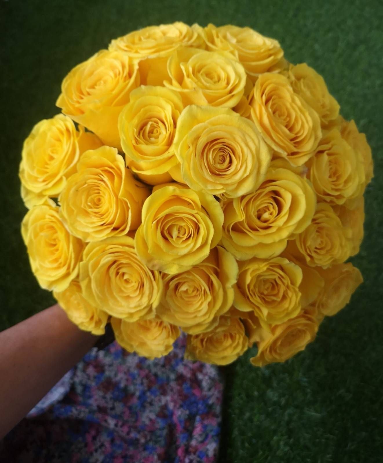 Un ramo redondo de rosas de color amarillo brillante sobre un fondo verde y cubierto de hierba.