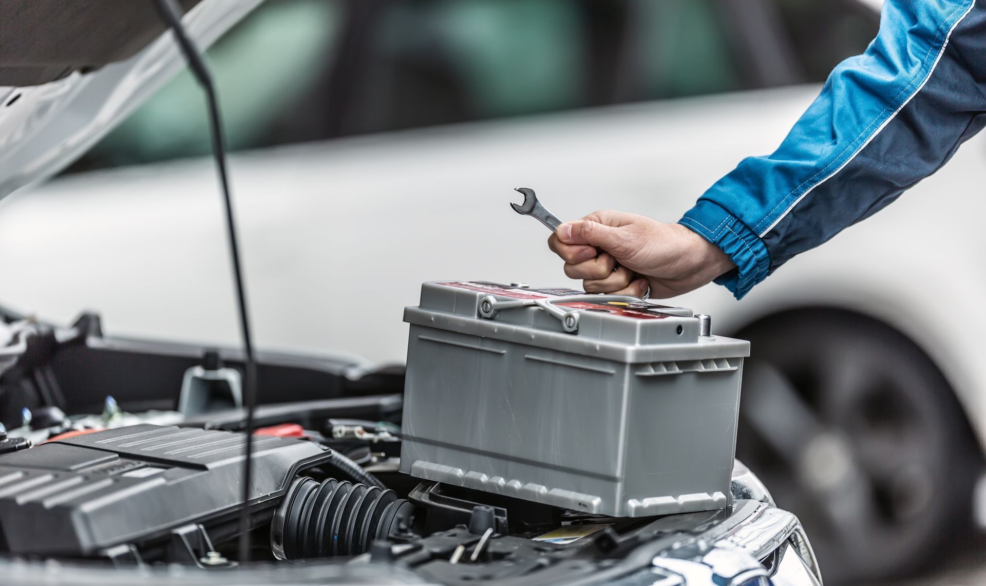 Une main posée sur une batterie de voiture et tenant une clé anglaise