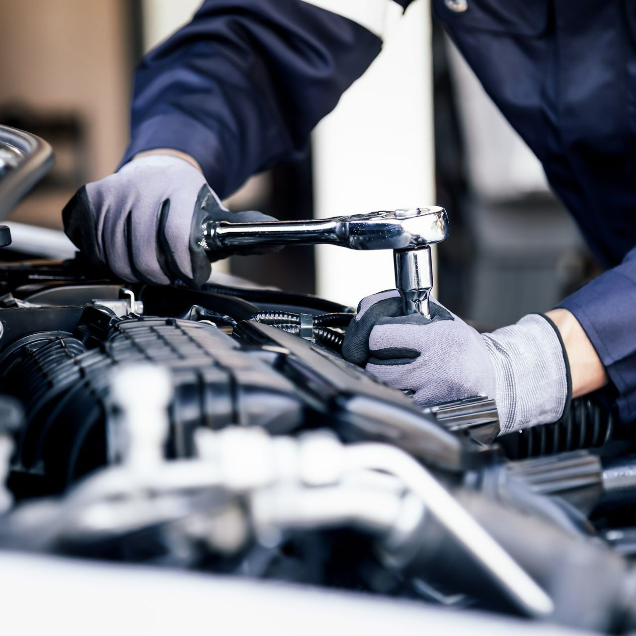 Des mains gantées utilisent un outil pour serrer un élément au niveau du moteur d'une voiture