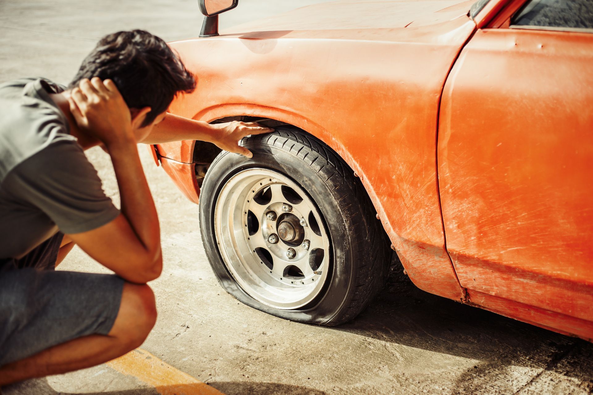 Un homme dépité regarde le pneu crevé de sa voiture orange