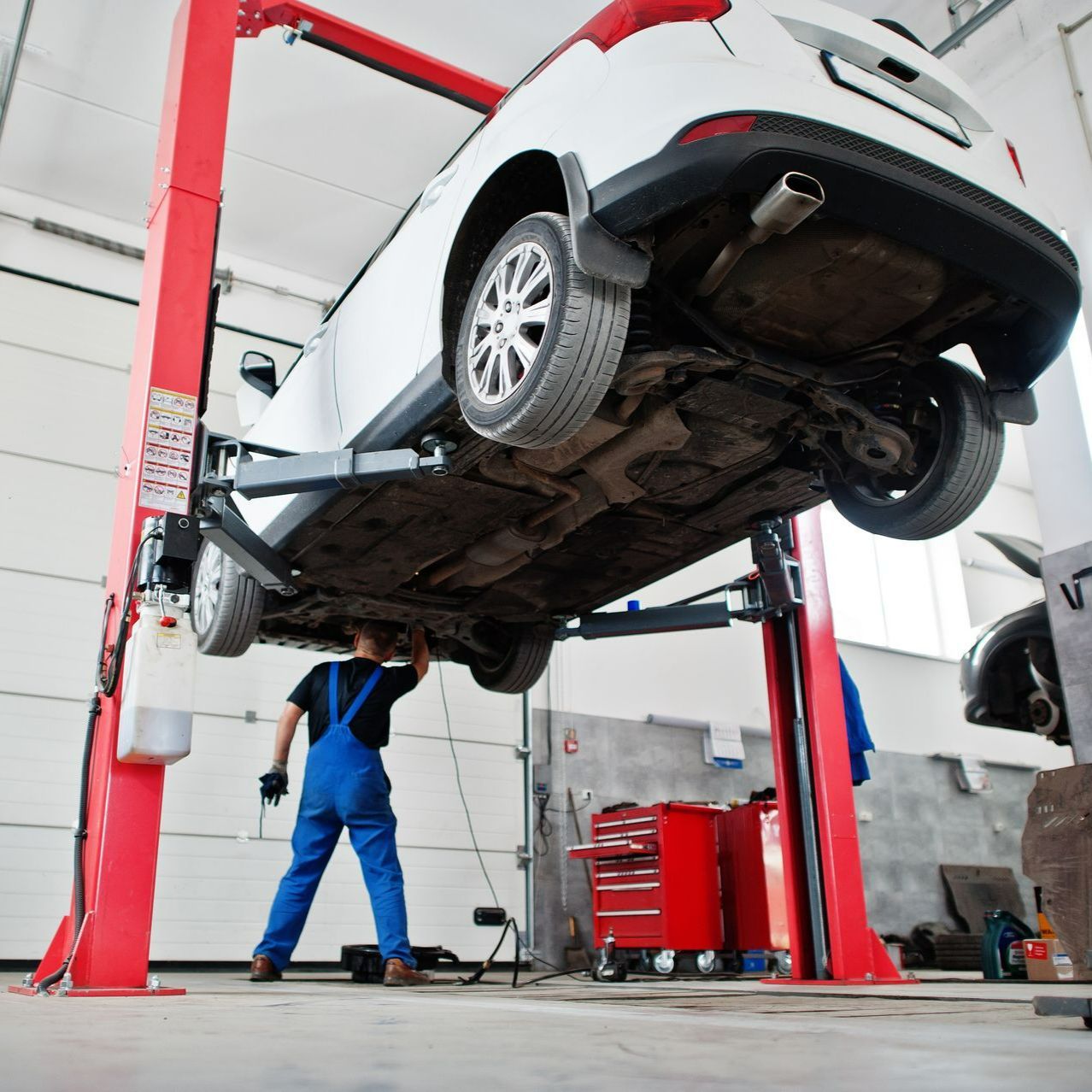 Un garagiste sous une voiture blanche suspendue dans un garage 