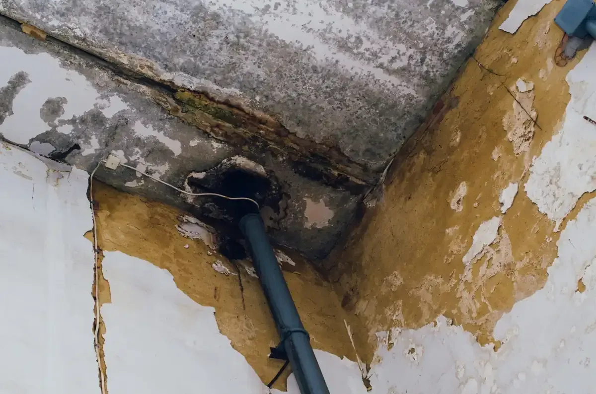 Persona arreglando tuberías bajo un fregadero blanco con una llave inglesa. Pared de azulejos grises.