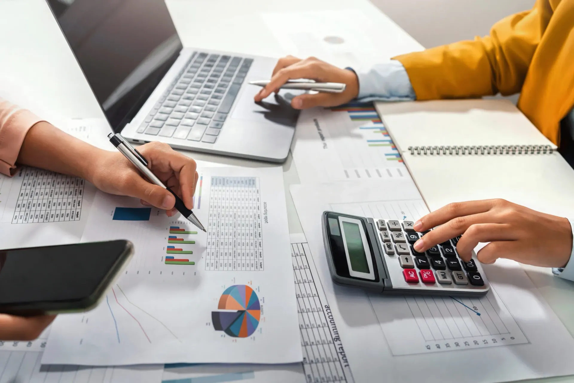 Manos trabajando con documentos, computadora portátil, calculadora y teléfono.