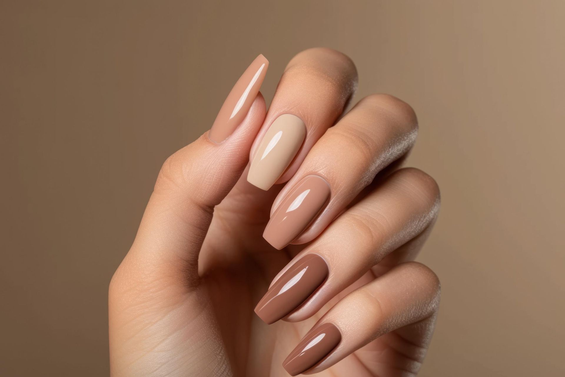 Un primer plano de la mano de una mujer con uñas largas y esmalte de uñas marrón.