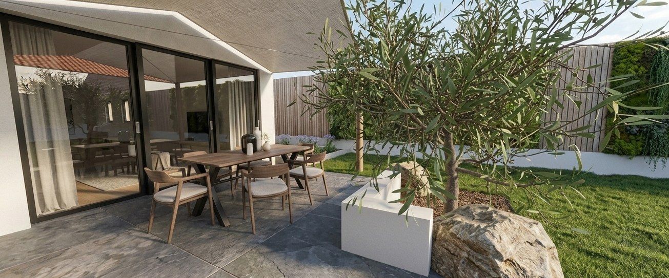 Terrasse avec salon de jardin, sol en carreaux de pierre, muret d'agrément, jeune olivier et rochers décoratifs en bord de pelouse