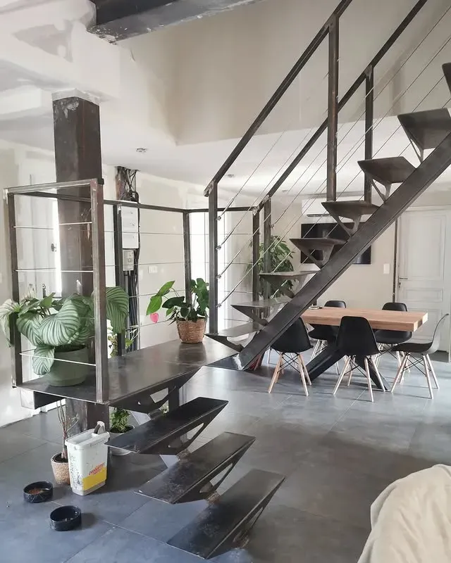 Intérieur moderne avec escalier en acier, coin repas et plantes en pot.