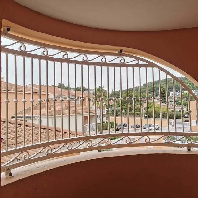 Rambarde métallique sur un balcon voûté offrant une vue sur les bâtiments et les arbres.