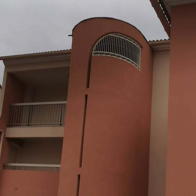 Immeuble d'appartements rose avec balcons et façade incurvée ornée d'une fenêtre décorative.