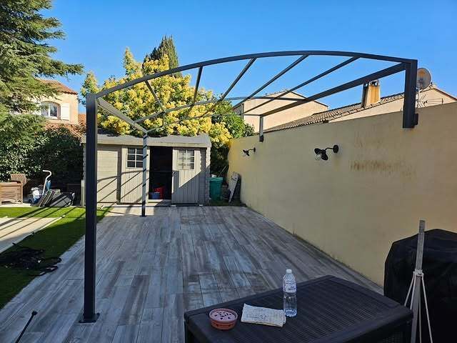 Pergola sur terrasse en bois dans le jardin, abri de jardin en arrière-plan, ciel bleu.