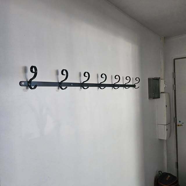 Un porte-manteau en métal noir à neuf crochets est fixé sur un mur blanc.