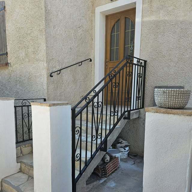 Extérieur d'un bâtiment avec une balustrade en fer noir menant à une porte en bois.