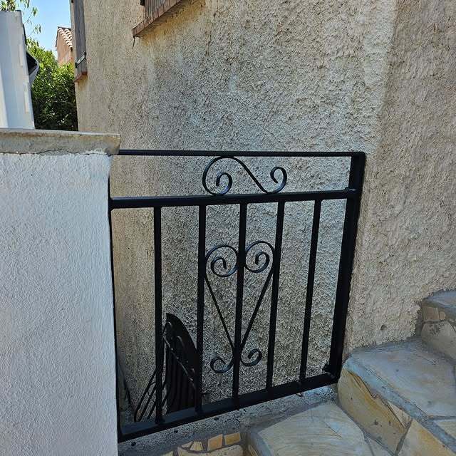 Portail en métal noir entre un mur texturé et des marches.