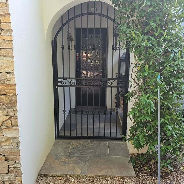 Un portail en fer forgé noir dans une porte cintrée donne sur une entrée sombre.