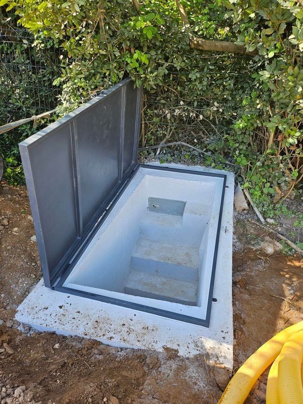 Cave ouverte en béton avec porte en métal gris et marches descendantes.