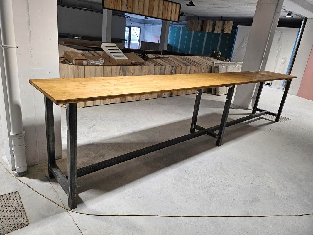 Longue table en bois avec des pieds en métal dans une pièce en béton.