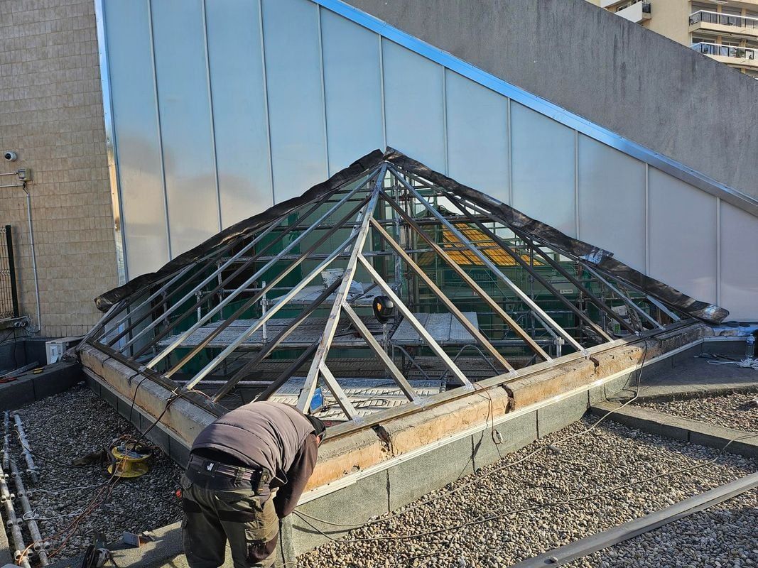 Un ouvrier répare une lucarne en forme de pyramide sur un toit plat.
