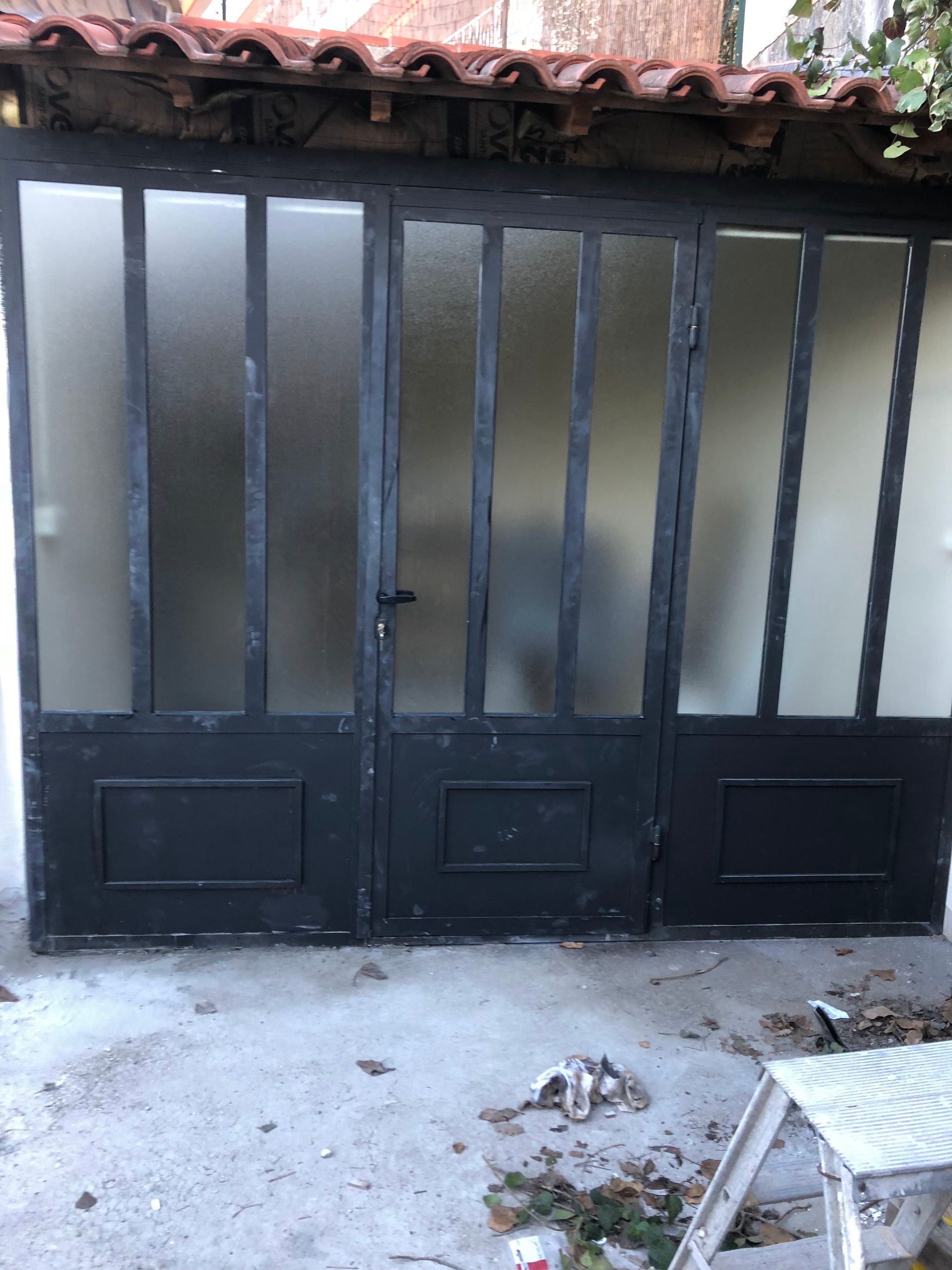 Portes vitrées à cadre métallique noir contre une surface en béton. Des panneaux de verre dépoli sont visibles.