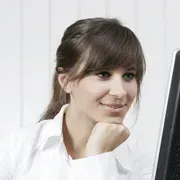 Una mujer está sentada frente a una pantalla de computadora con la mano en la barbilla.