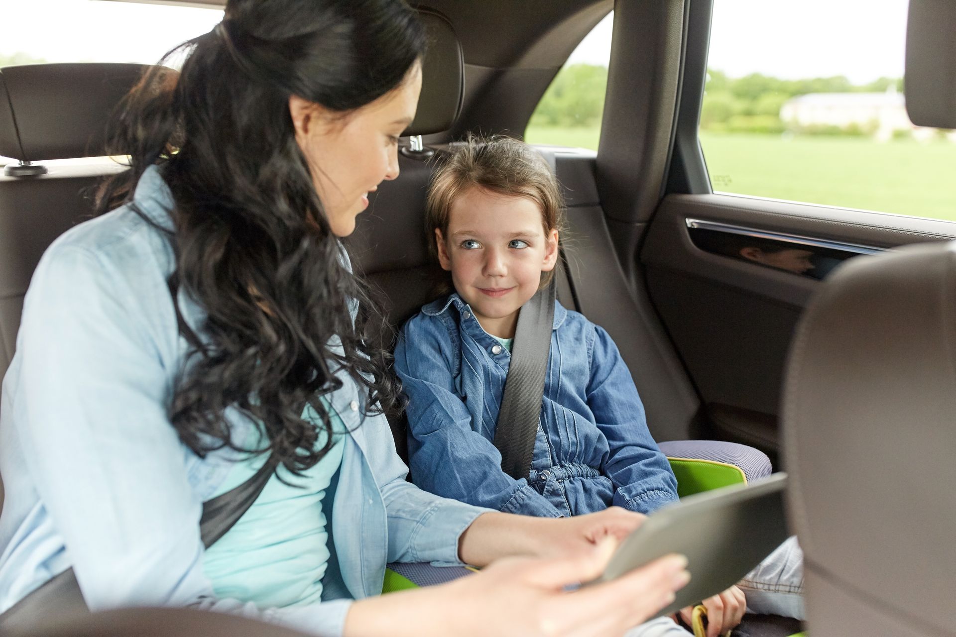 Une femme et un enfant dans une voiture ; la femme tient une tablette, l'enfant sourit, tous deux sont attachés.
