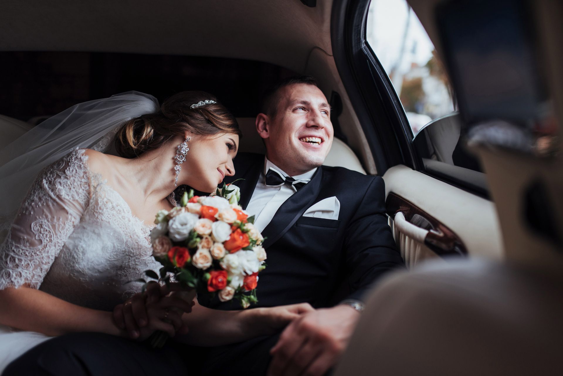 Les mariés dans une voiture après la cérémonie, la mariée avec son bouquet et son voile, le marié souriant.