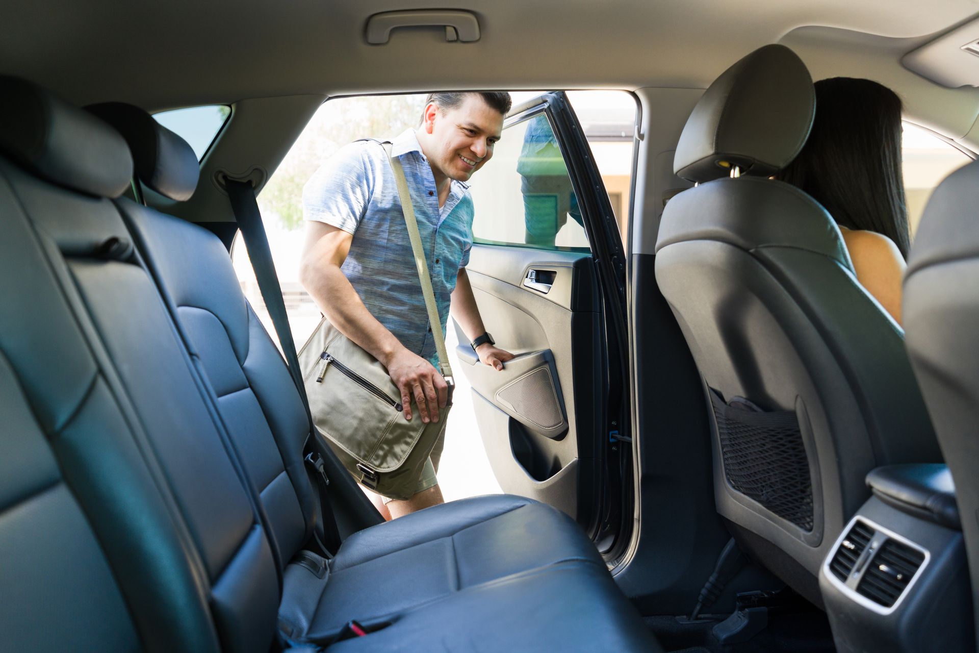 Un homme sort de la banquette arrière d'une voiture, un sac à la main. Une autre personne est assise dans la voiture.