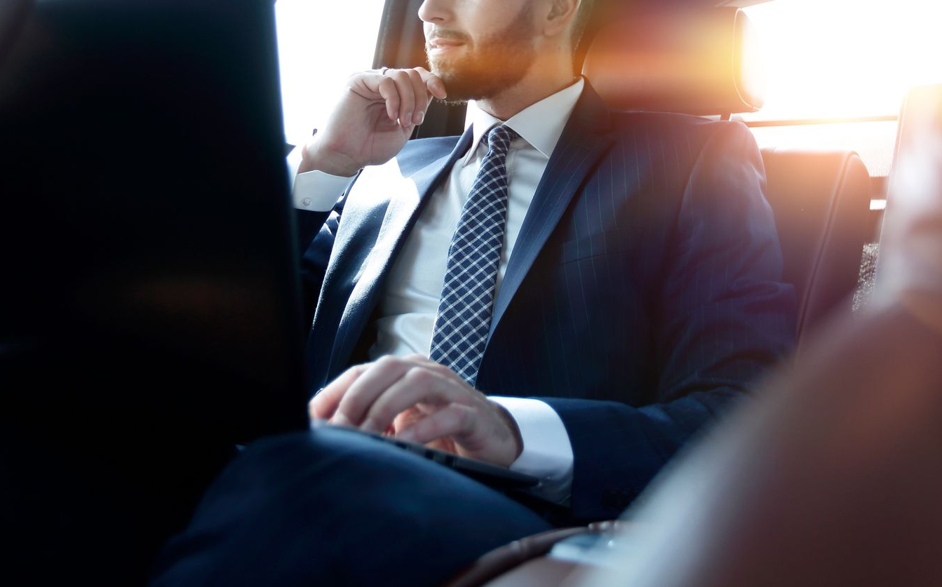 Un homme en costume, assis dans une voiture, regarde par la fenêtre.