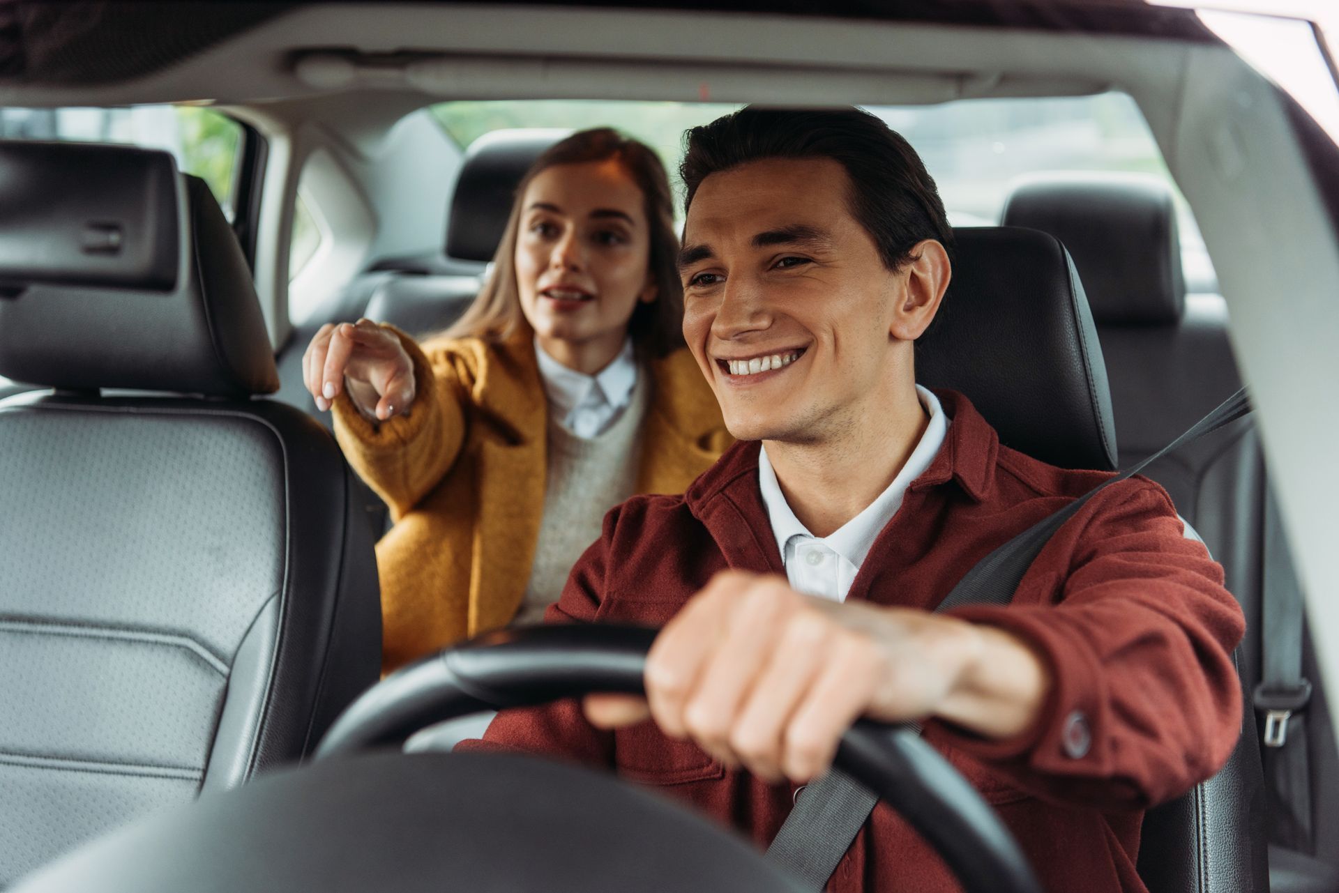 Un homme conduit en souriant tandis qu'une passagère désigne du doigt. À l'intérieur d'une voiture.
