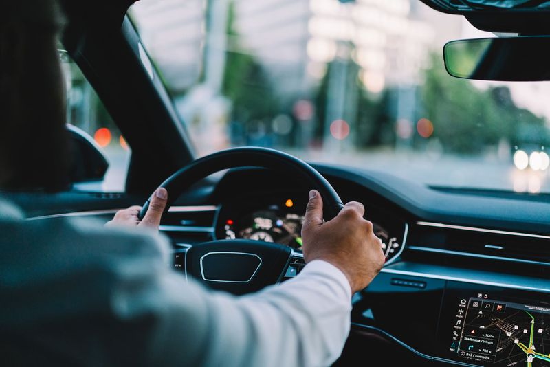 Les mains d'une personne tenant un volant. Vue intérieure d'une voiture avec un paysage urbain visible à travers le pare-brise.