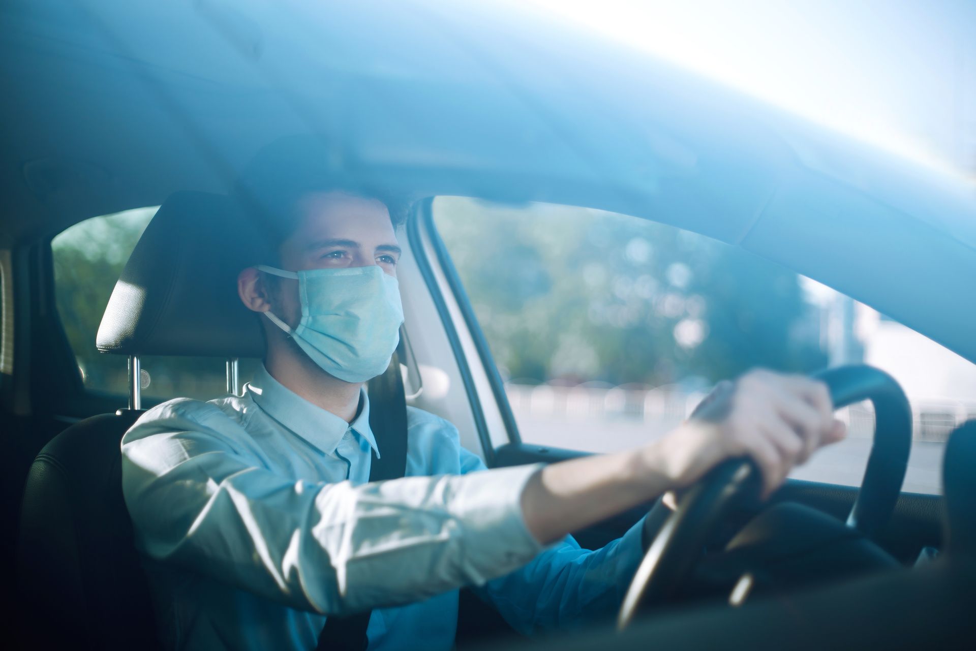 Un homme portant un masque conduit une voiture, en plein soleil.