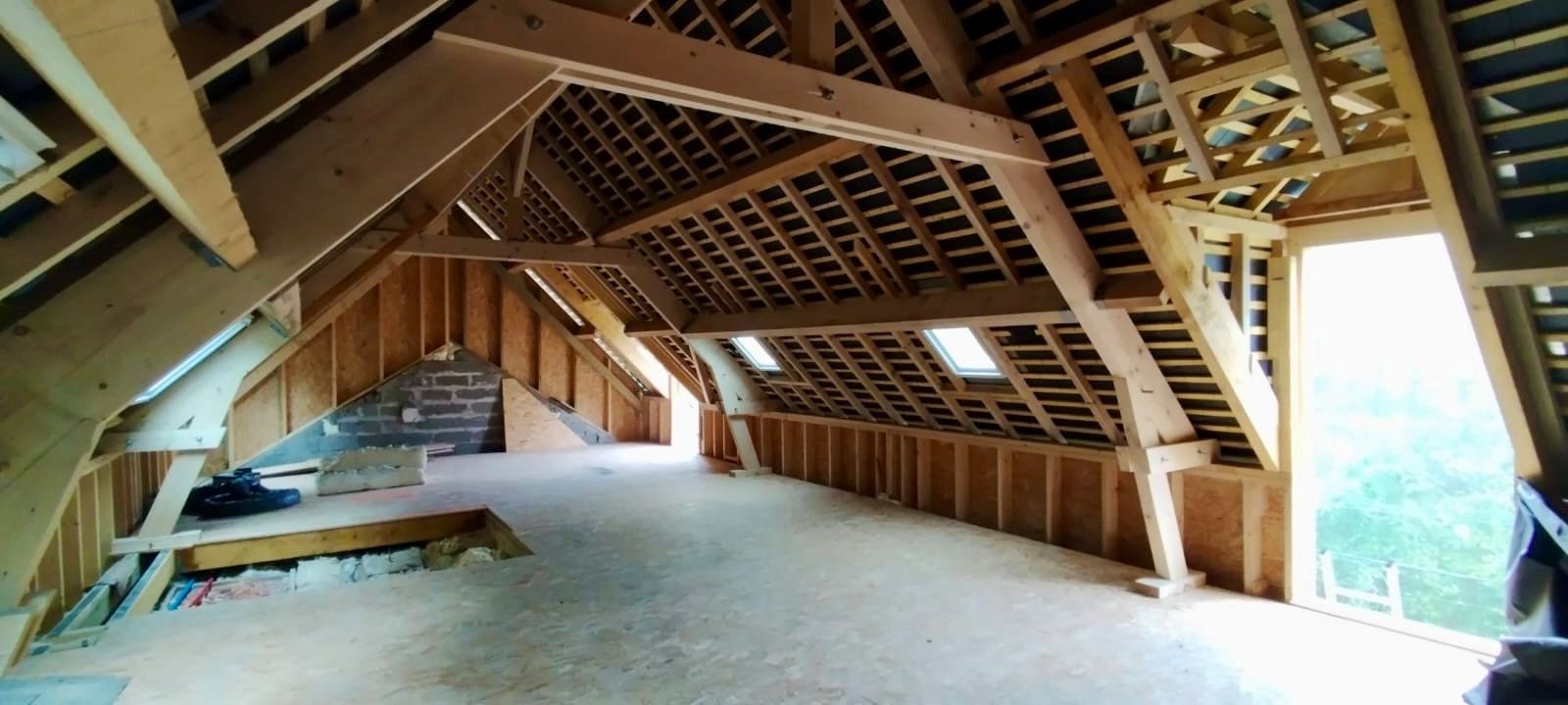 Vue intérieure d'un grenier inachevé avec poutres et charpente en bois.