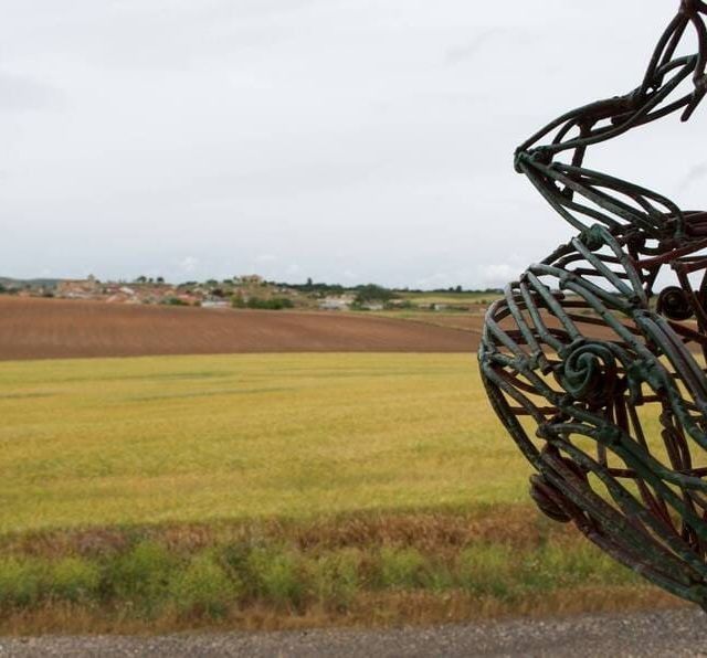 Una escultura de una persona parada frente a un campo.