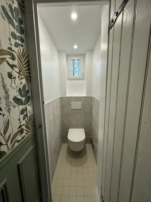 Une personne installe un robinet de douche circulaire chromé sur un mur carrelé hexagonal gris clair.