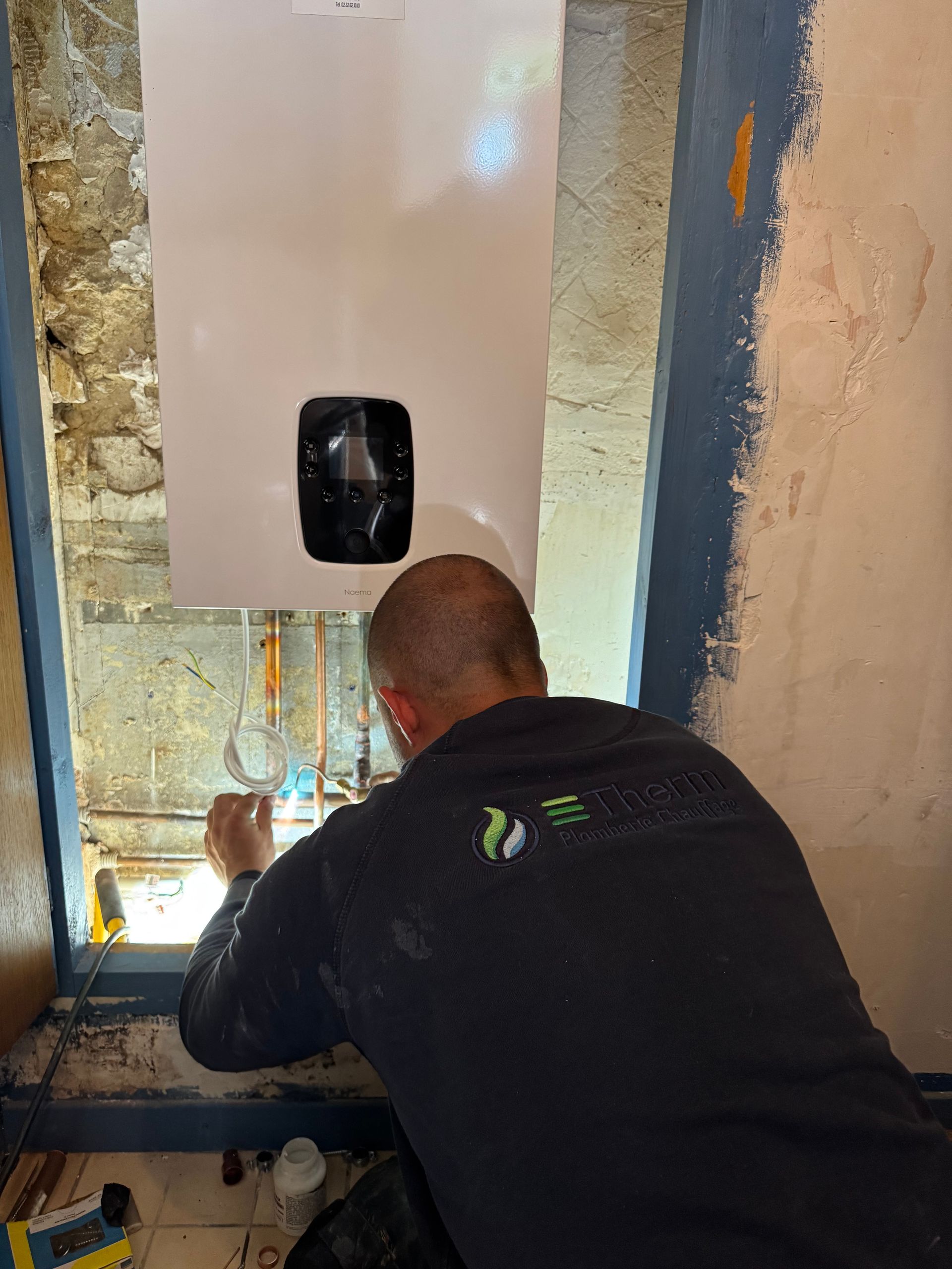 Une chaudière à gaz murale blanche avec ses tuyaux, se détachant sur un fond bleu foncé uni.