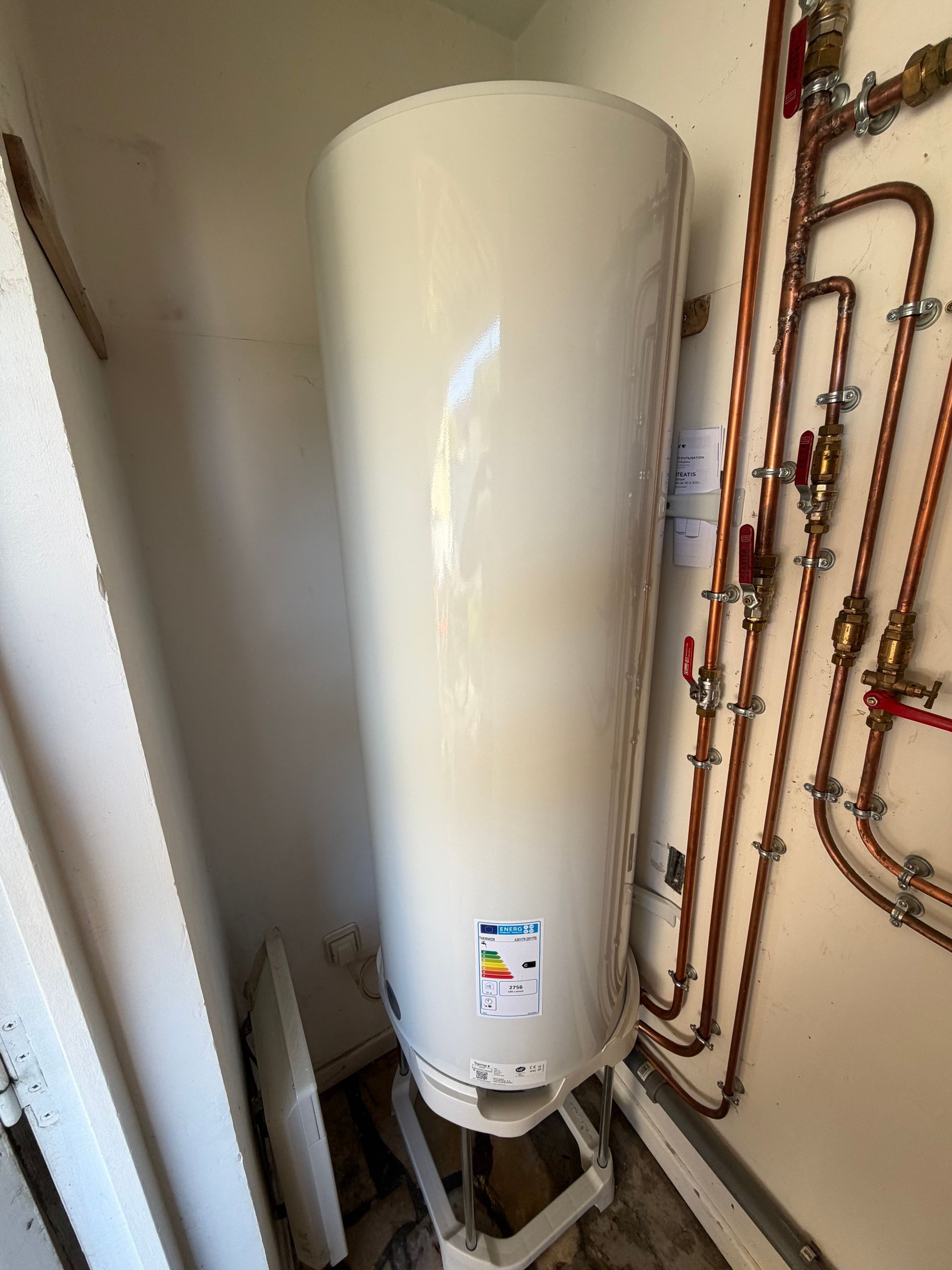 Une main gantée tient un tuyau d'évacuation d'évier qui goutte pendant qu'elle effectue des travaux d'entretien sous un lavabo blanc.