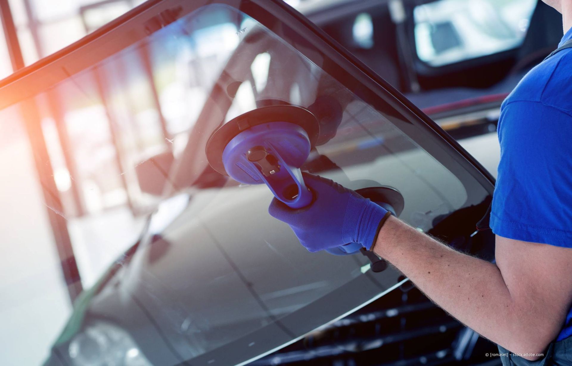 Ein Mechaniker in blauem Overall, der Kaffee und ein Tablet in der Hand hält, lächelt in einer Werkstatt.