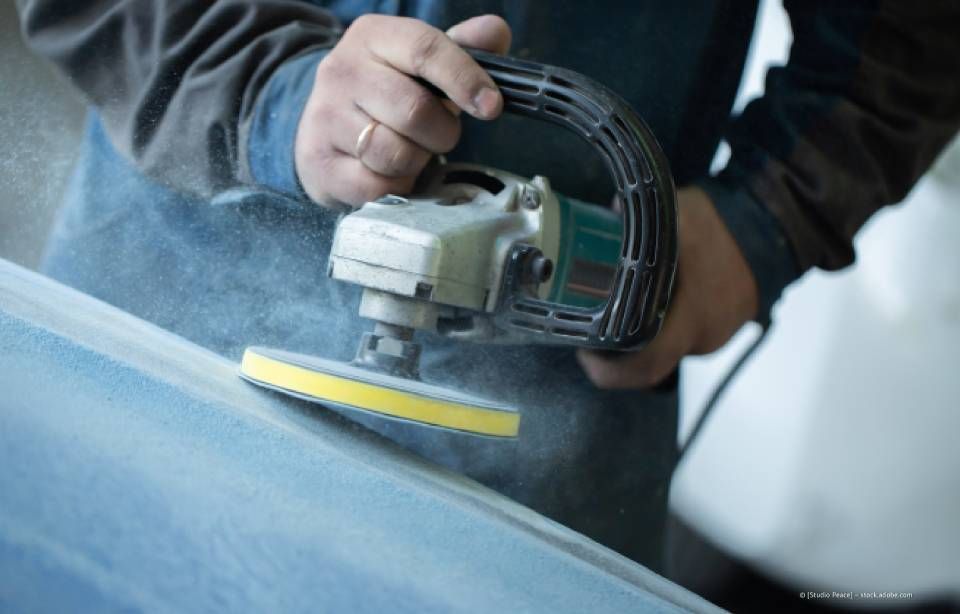 Eine Person benutzt einen elektrischen Schleifer auf einer blauen Oberfläche und erzeugt dabei Staub.