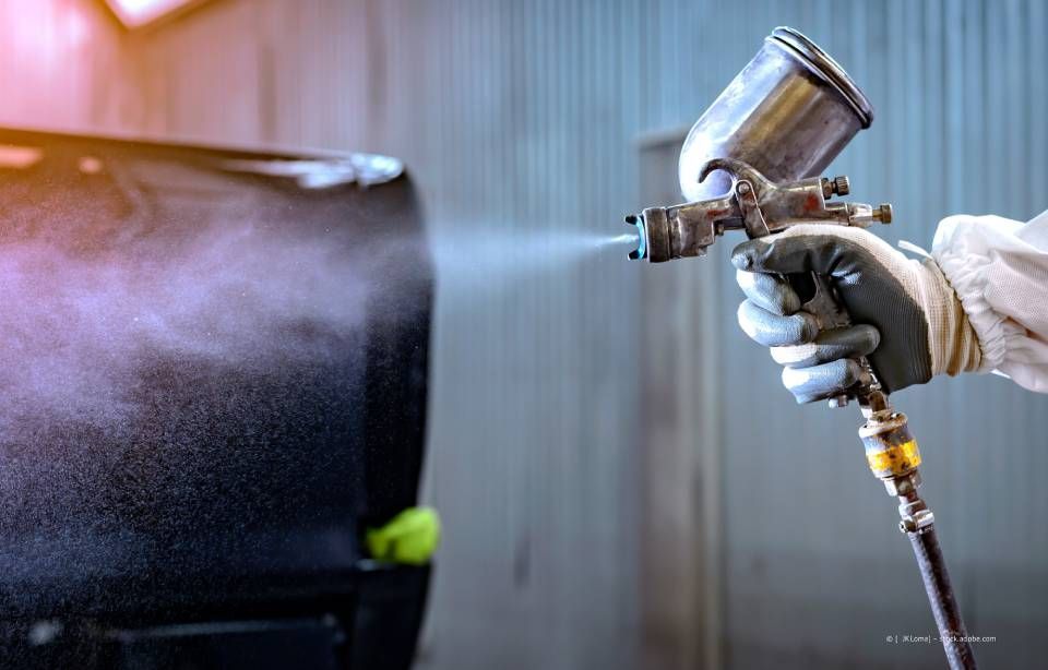 Eine Person in Schutzkleidung besprüht ein Auto mit einer Farbpistole.