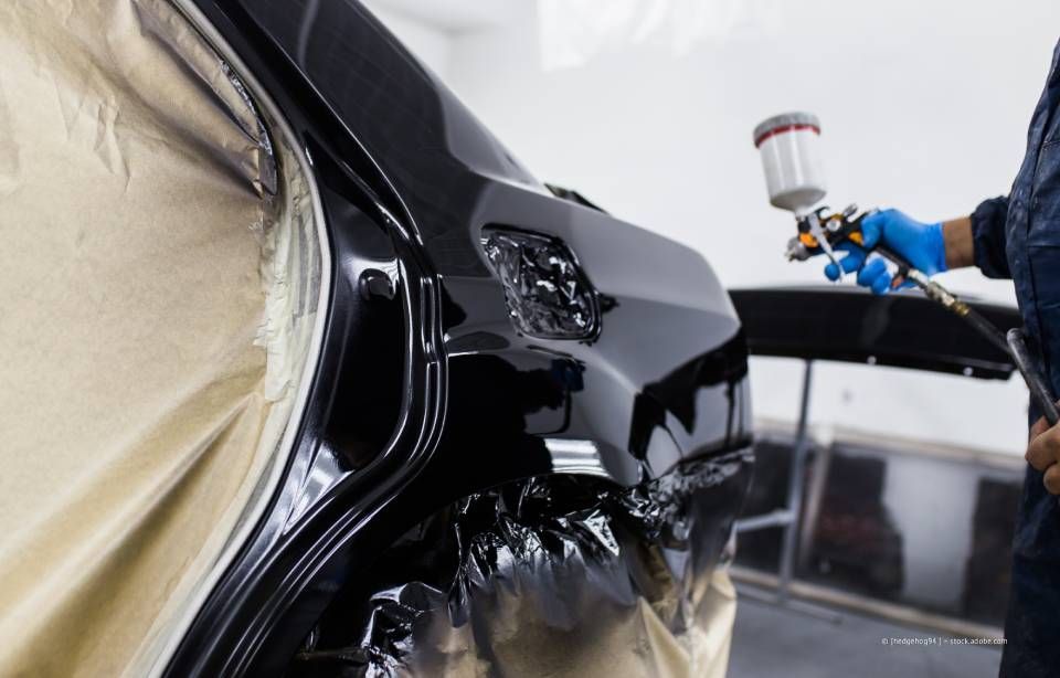 Eine Person bringt mit Hilfe eines Heißluftföns und eines Rakels eine Vinylfolie auf einem roten Auto an.