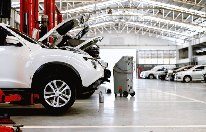 In einer hell erleuchteten Autowerkstatt werden Autos gewartet; die Motorhauben sind geöffnet.