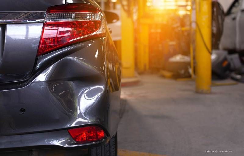 Zwei Männer begutachten den Schaden an der Seite eines weißen Autos, möglicherweise nach einem Zusammenstoß. Einer zeigt auf einen Kratzer.