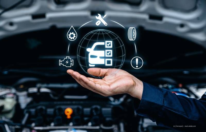 Eine Hand hält ein Autosymbol mit Diagnosesymbolen vor einem geöffneten Automotor.