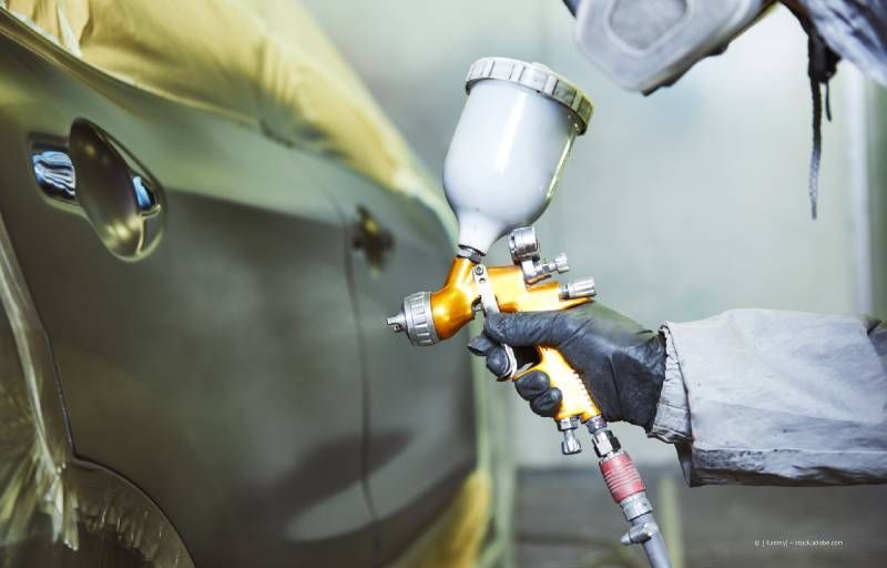 Eine Person, die Schutzkleidung trägt, lackiert ein Auto mit einer Spritzpistole.