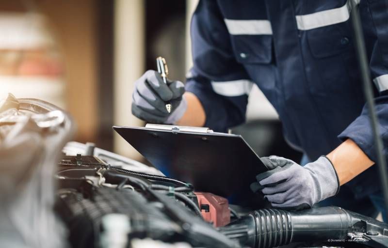 Eine Person, die Schutzkleidung trägt, lackiert ein Auto mit einer Spritzpistole.