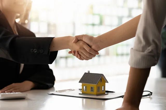 Una mujer le da la mano a un hombre delante de una casa modelo.