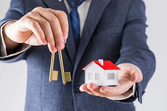 Un hombre con traje sostiene una maqueta de casa y llaves.