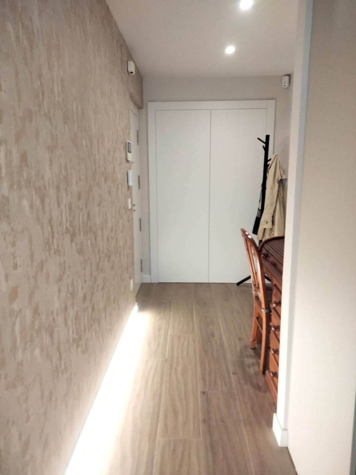 Un pasillo con suelo de madera y una puerta blanca.