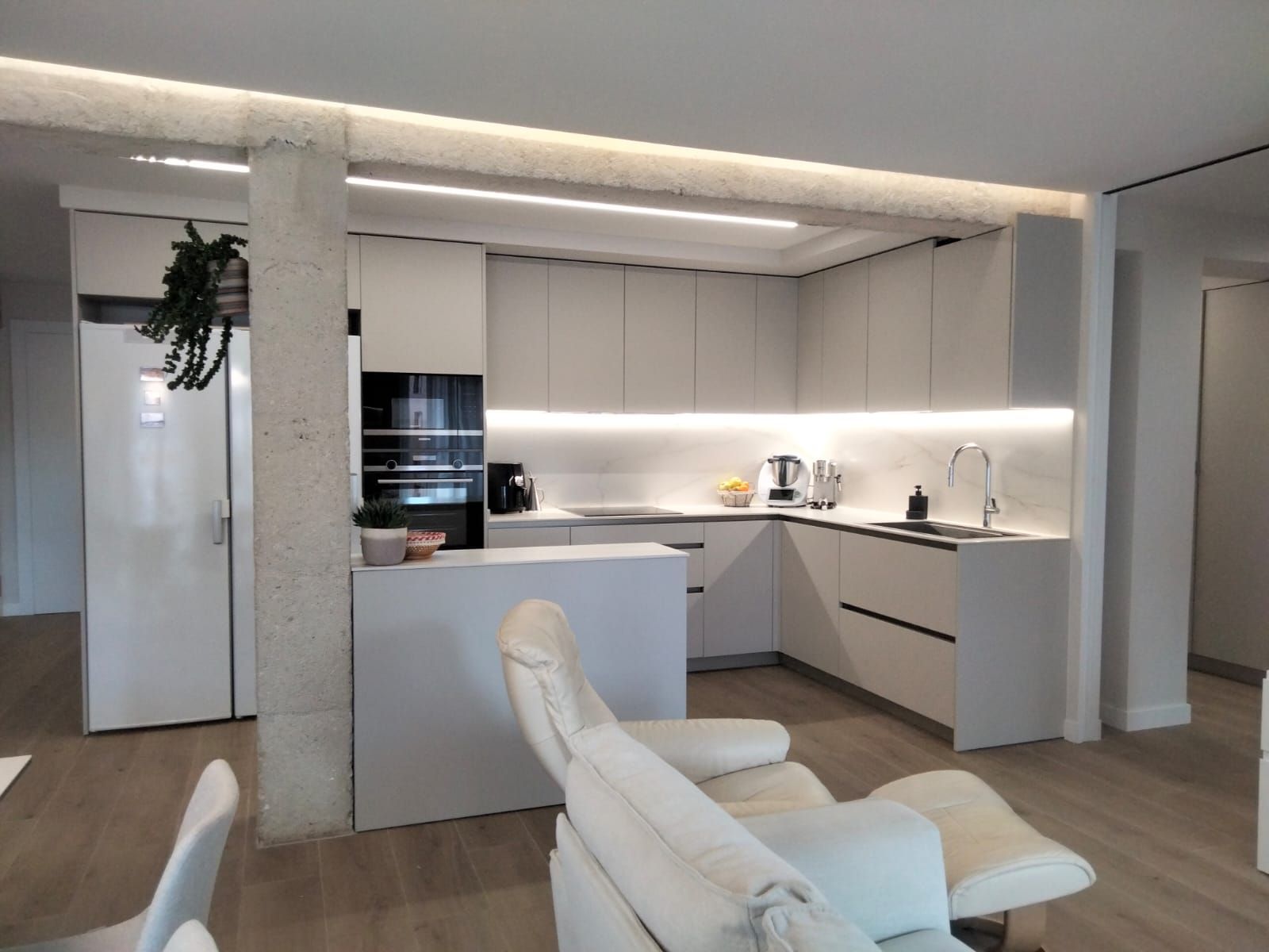 Una cocina con gabinetes blancos y una silla blanca.